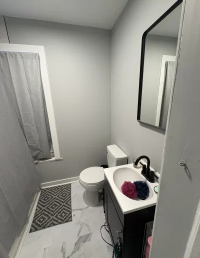 Modern small bathroom with grey walls, white toilet, vanity sink, and marble-style flooring