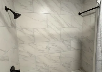 Tiled bathtub and shower area with white marble-style wall tiles and black fixtures