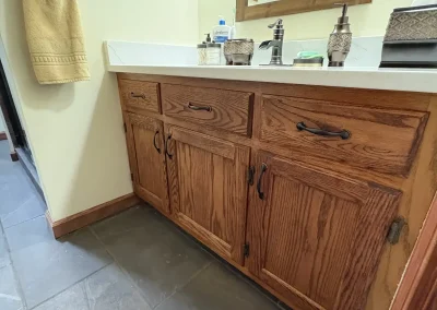 Rustic bathroom vanity with oak wood cabinets, white countertop, and mounted mirror