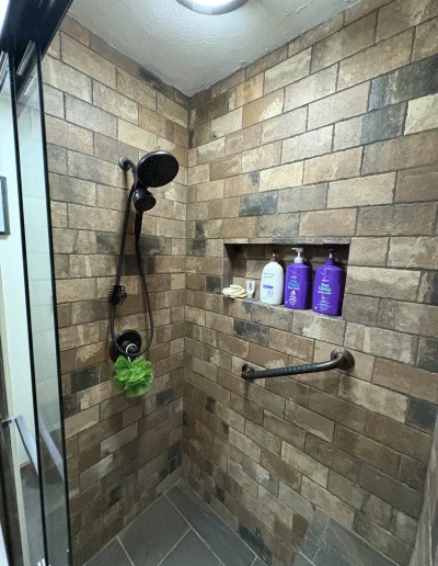 Finished stone-tiled shower with dual showerheads, grab bar, and recessed shelf