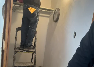 Contractor standing on ladder during closet renovation, installing shelving and lighting