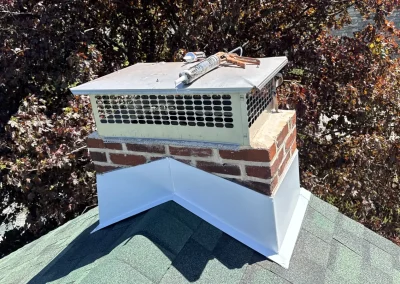 Repaired brick chimney with new metal cap and white flashing on asphalt shingle roof