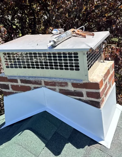 Repaired brick chimney with new metal cap and white flashing on asphalt shingle roof