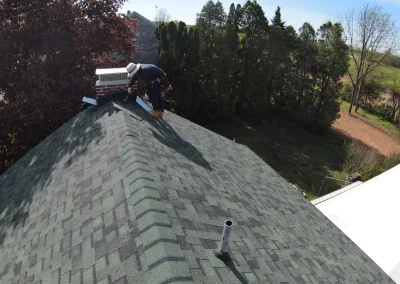 Roofer sealing chimney flashing on asphalt shingle roof during repair process