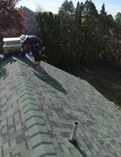Roofer sealing chimney flashing on asphalt shingle roof during repair process