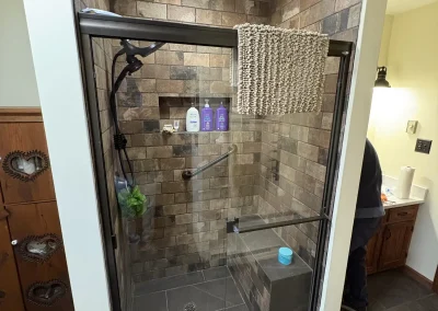 Finished walk-in shower with stone tile walls, glass door, and built-in shelving