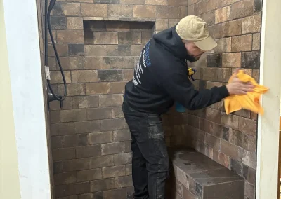 Contractor cleaning newly tiled stone shower with built-in bench during renovation