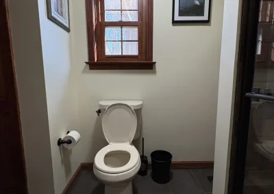 Modern bathroom with toilet under wooden-framed window and framed wall art