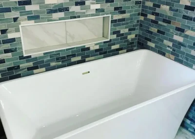 Freestanding bathtub with marble floor and teal mosaic wall tiles during a modern bathroom remodel.