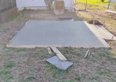 Newly poured concrete foundation slab drying beside a residential home.