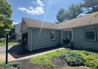 Front view of renovated home with new grey siding, brown shingle roof, and landscaped garden walkway on a sunny day.
