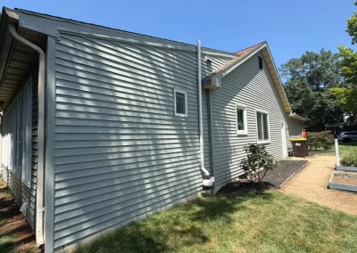 Residential exterior with new vinyl siding, gutter system, and landscaped garden path on a sunny day.
