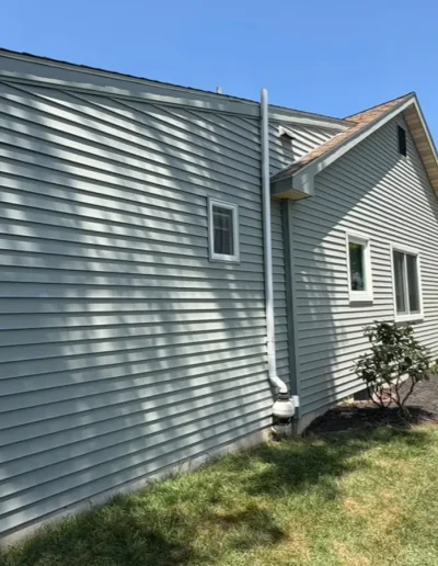 Residential exterior with new vinyl siding, gutter system, and landscaped garden path on a sunny day.