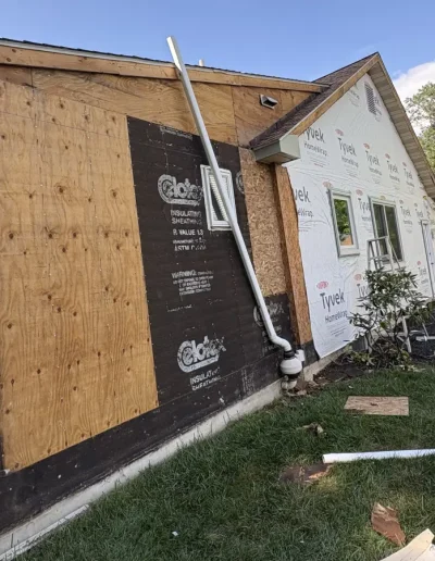 House exterior during renovation showing plywood sheathing and Tyvek HomeWrap ready for new siding installation.