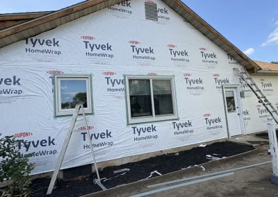 Home exterior wrapped in Tyvek HomeWrap with window frames and ladders prepared for siding installation.