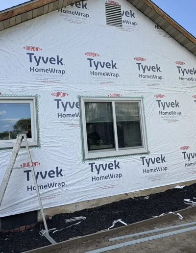 Home exterior wrapped in Tyvek HomeWrap with window frames and ladders prepared for siding installation.