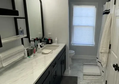 Luxury bathroom with black vanity, marble countertop, large mirror, and marble-style flooring.