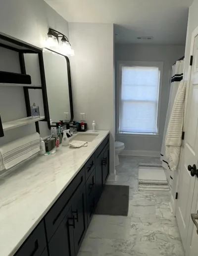Luxury bathroom with black vanity, marble countertop, large mirror, and marble-style flooring.