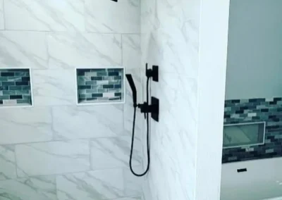 Marble shower with black fixtures, mosaic floor tiles, and built-in wall niches beside a freestanding bathtub.