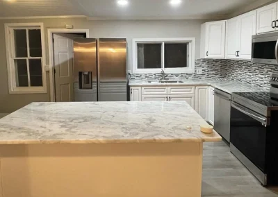 Modern kitchen with marble countertops, stainless steel fridge and oven, and white cabinets with mosaic tile backsplash.