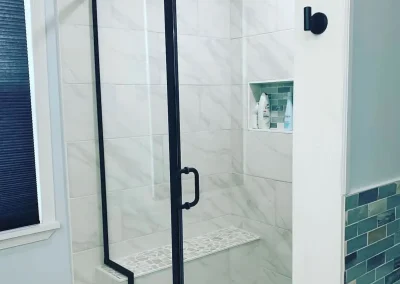 Modern walk-in shower with black-framed glass door, marble wall tiles, and mosaic tile floor.