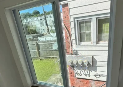 Newly installed double-pane window with wooden sill showing view of brick wall and backyard outside.