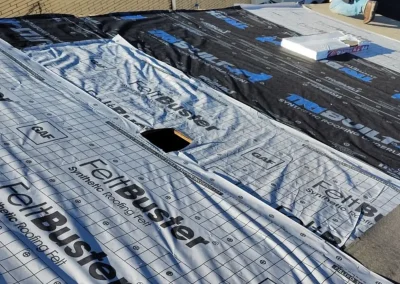 Roofer installing GAF FeltBuster synthetic underlayment on a roof before adding shingles.