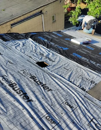 Roofer installing GAF FeltBuster synthetic underlayment on a roof before adding shingles.