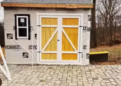 Partially finished shed with barn doors and exterior sheathing wrap during construction.