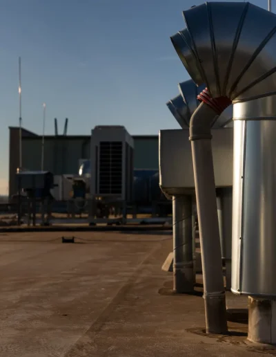 Rooftop HVAC ventilation system with large metal exhaust ducts and pipes under natural daylight, part of a commercial building’s climate control infrastructure.