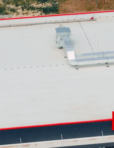 Aerial view of a commercial building roof with HVAC ductwork and ventilation systems, bordered by a red trim along the rooftop edge.