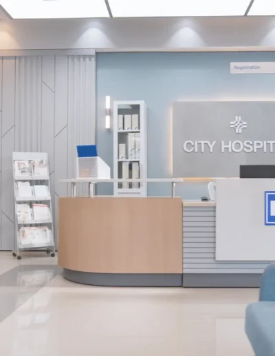 Modern hospital reception area with a clean, minimalist design featuring a curved desk, soft blue accents, seating area, and clear signage for registration and cashier counters.