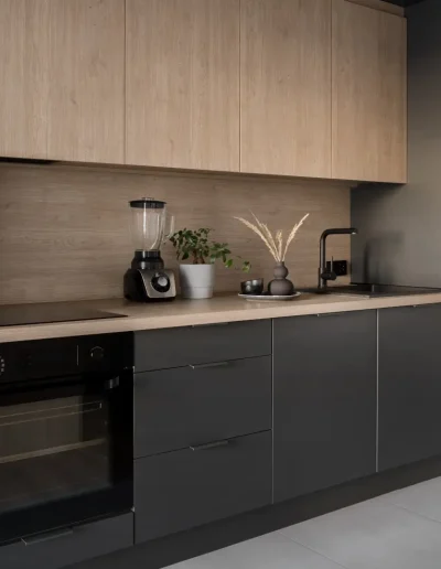 Modern compact kitchen with matte black lower cabinets, light wood upper units, minimalist appliances, and subtle décor for a sleek, contemporary look.