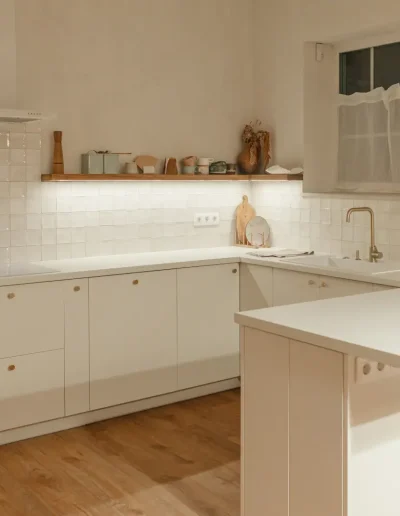 Modern minimalist kitchen with white cabinetry, wood flooring, tiled backsplash, and under-shelf lighting, featuring a cosy Scandinavian-inspired design.