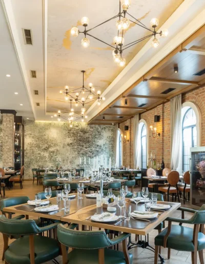 Elegant restaurant interior with a mix of classic and modern design, featuring brick walls, arched windows, chandeliers, and neatly set dining tables with stylish seating.