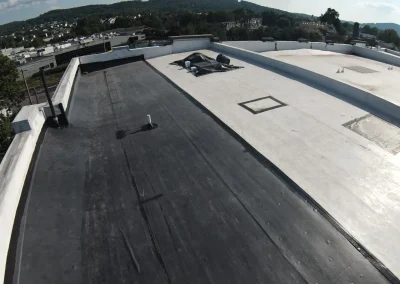 Aerial drone view of a large flat commercial rooftop showing existing EPDM membrane and TPO white parapet sections with HVAC equipment and drains visible