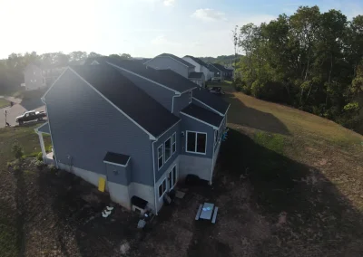 Aerial drone view of a newly completed dark charcoal asphalt shingle roof on a large two-story residential home surrounded by green trees and open yard