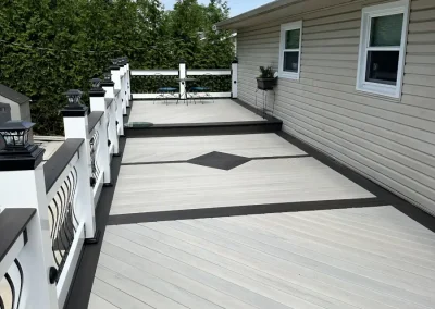 Daytime view of a multi-level composite deck in light gray and charcoal with decorative diamond inlay, ornate black metal balusters, and solar post cap lights