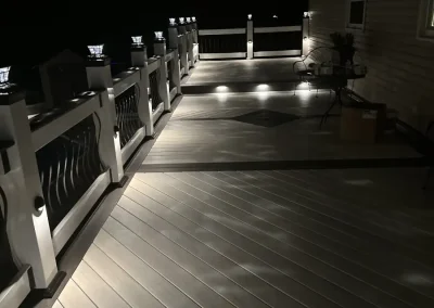 Multi-level composite deck illuminated at night with LED step lights, solar post cap lights, and decorative curved metal baluster railings