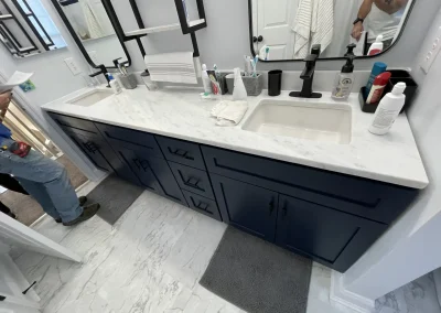 Close-up of renovated bathroom double vanity with navy shaker cabinets, white marble countertop, dual undermount sinks, and matte black hardware and faucets