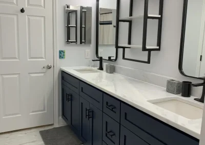 Renovated bathroom featuring navy blue double vanity with marble countertop, dual undermount sinks, black fixtures, arched mirrors, and marble-look tile flooring