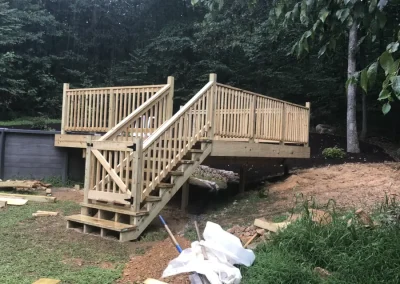 Pressure-treated wood pool platform deck with white spindle railings and staircase built on a wooded hillside lot, still under construction