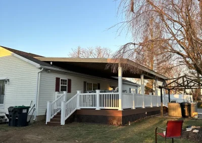 Side view of a low-profile composite deck with white vinyl railings attached to a mobile home, featuring a broad covered roof addition overhead