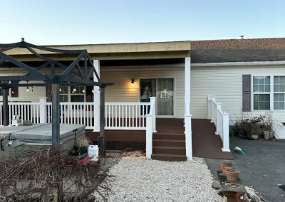 Newly completed covered front porch and deck addition with composite decking, white vinyl railings, pergola structure, and gravel landscaping