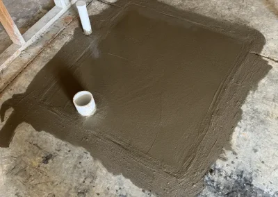 Freshly poured concrete floor patch covering newly installed underground plumbing rough-in with PVC drain pipes protruding for future fixture connections
